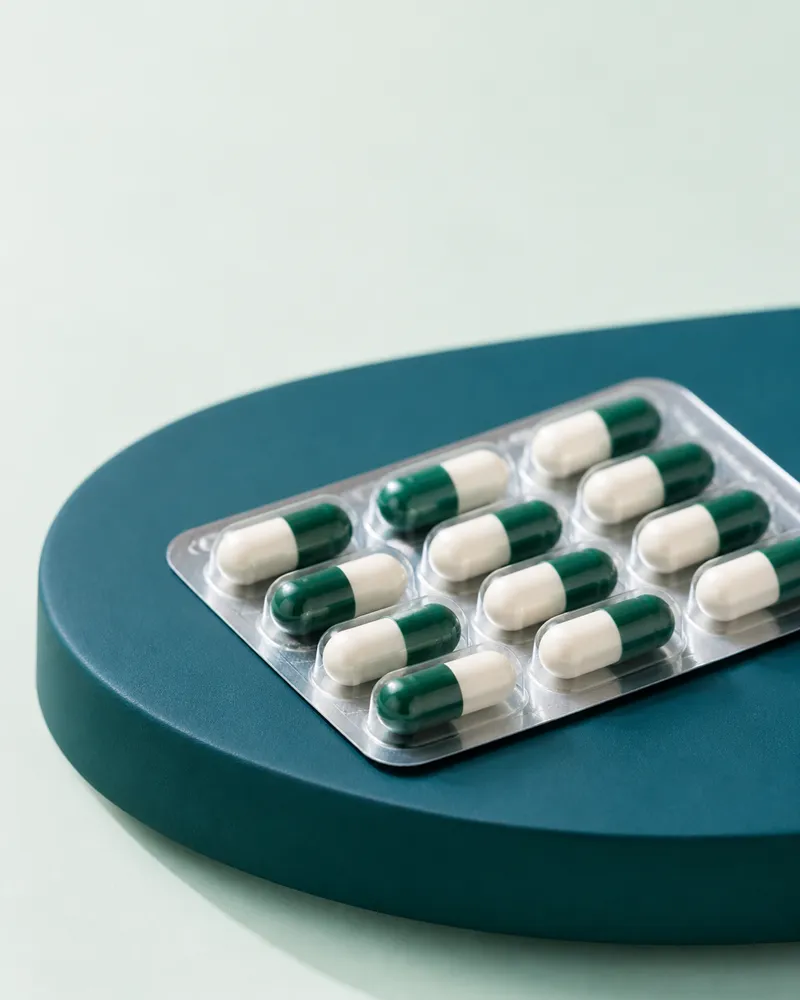 Green and white capsules in clear blister packaging on a teal plinth
