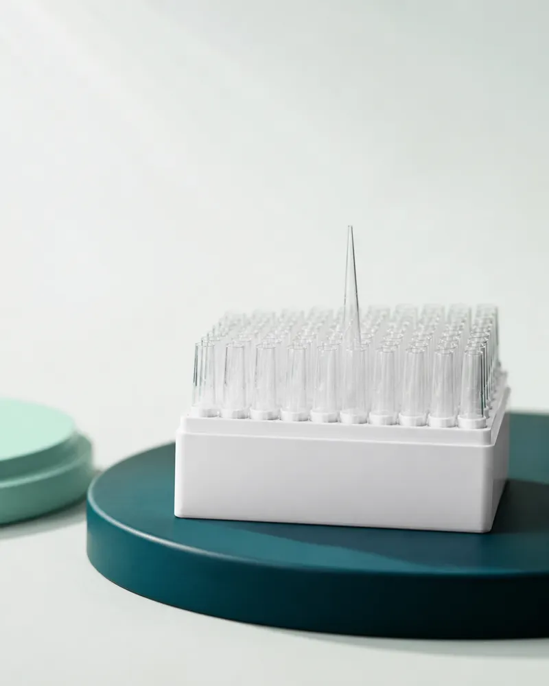 White rack of clear laboratory pipette tips on a teal plinth